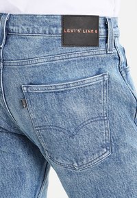 Ljusblå denimjeans med en sydd bakfick och en svart läderlapp med "LEVI'S LINE 8" präglat på midjan.