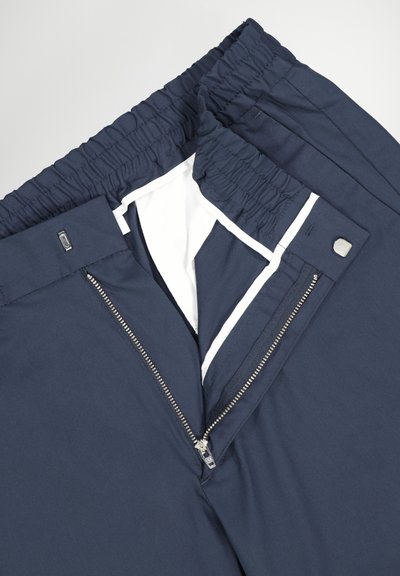 Marineblauwe broek met een brede elastische tailleband, uitgerust met een ritssluiting en knoopsluiting, met witte voering zichtbaar bij de opening.