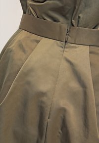 Oliivinvihreä mekko, jossa on teksturoitu pinta, leveä vyö, laskoskuvio ja piilotettu sivuvetoketjutyyli.