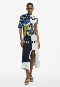 Kleid in Blau, Schwarz und Weiß mit asymmetrischem Design, großen grafischen Drucken und einem hohen Schlitz. Hergestellt aus leichtem Stoff, mit kurzen Ärmeln.