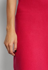 Vänsterhand med svart nagellack som vilar mot ett texturerat ljusrosa tygplagg.