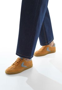 Sneakers in rete arancioni con dettagli grigio chiaro e suole in gomma. Abbinati a pantaloni larghi in denim blu.