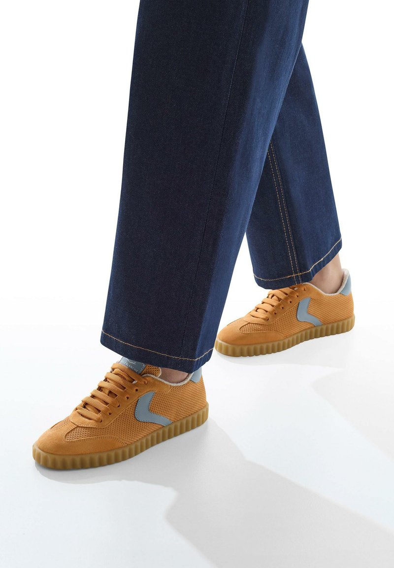 Sneakers in rete arancioni con dettagli grigio chiaro e suole in gomma. Abbinati a pantaloni larghi in denim blu.