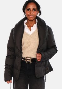 Svart dunsjakke med høy krage, blank finish og ribbet tekstur. Brukt over en beige genser, kombinert med svarte jeans med høyt liv og belte.