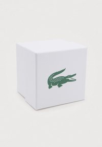 White textured box with a green crocodile logo printed on the front side against a plain background.
