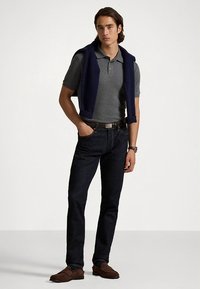 Γκρι πόλο πουκάμισο, ναυτικό πουλόβερ κρεμασμένο στους ώμους, σκουρόχρωμα τζιν, καφέ μοκασίνια, ασημένιο ρολόι, κλασική εφαρμογή, ομαλή υφή.