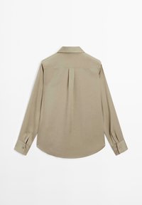 Chemise beige à manches longues avec un pli dans le dos, des poignets boutonnés et un col classique, présentée à plat vue de dos sur fond blanc.