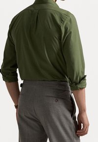 Groen katoenen shirt met opgerolde mouwen en een plooi, gecombineerd met grijze textuurbroek met een achterzak en knoopdetail.