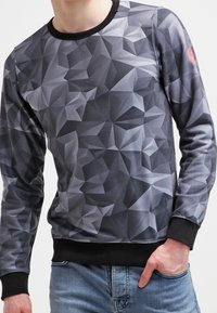 Sweatshirt à manches longues avec un motif géométrique noir et gris. Tissu doux avec des poignets et un col côtelés. Coupe décontractée.
