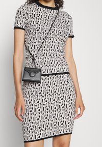 Jersey jurk van stretchmateriaal met een monochroom geometrisch patroon, korte mouwen, aansluitende silhouet en contrasterende zwarte afwerking; gecombineerd met een kleine zwarte tas.