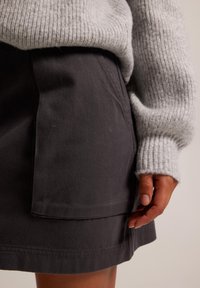 Grå denimkjol med frontfickdetalj, kombinerad med en ljusgrå stickad tröja som visar ribbad textur och mjukt tyg.