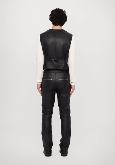 Gilet en cuir noir avec un dos ceinturé, associé à un pantalon en cuir noir assorti avec des zips sur les côtés et une coupe ajustée.