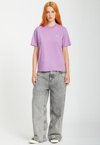 T-shirt en coton violet à manches courtes et col rond, associé à un jean en denim gris clair ample et des baskets noires.