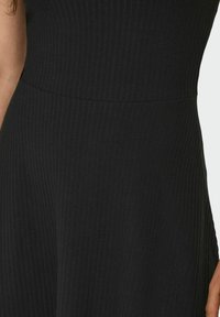 Zwarte ribstof jurk met details van de taille naad en gedeeltelijk zicht op de arm van de persoon aan beide zijden.