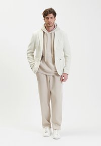 Blazer bianco su un hoodie beige e pantaloni a costine abbinati, abbinati a sneakers bianche. Tessuto morbido con una vestibilità su misura.