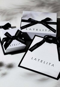 Tre scatole regalo bianche con dettagli neri, dotate di nastri neri e con il logo "LATELITA" stampato in caratteri bold su ciascun lato della scatola.