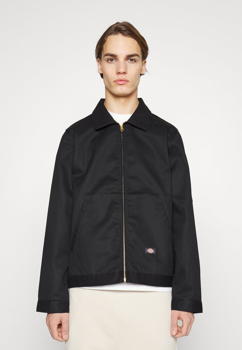 Giacca nera con zip, colletto classico, due tasche frontali e un piccolo logo sul lato sinistro in basso. Realizzata in tessuto solido e liscio.