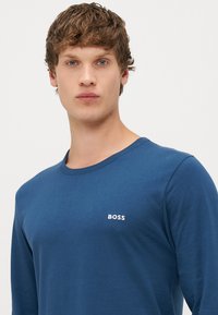 Modrá dlhá rukávová košeľa vyrobená z jemnej bavlny, s okrúhlym výstrihom a malým bielym logom 'BOSS' na ľavej hrudi.