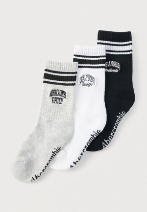 Trīs pāri kuģniecības zeķu pelēkā, baltā un melnā krāsā ar rilētu tekstūru un kontrastējošām svītru dizainiem augšpusē ar izšūtiem logotipiem.