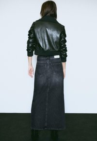 Veste bomber en cuir noir avec des poignets côtelés, associée à une longue jupe en denim foncé comportant deux poches arrière et une silhouette droite.
