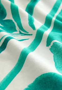 Bavlněná látka s bílým základem a vzorem zelených štětcových tahů. Textura je hladká, se viditelnými záhyby a sklady.