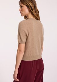 Beżowy sweter z krótkim rękawem, wykonany z miękkiego materiału, z prążkowanym dołem i gładką fakturą, w zestawie z czerwonymi, zwiewnymi spodniami.