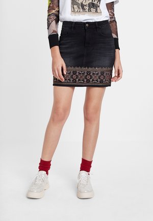 Mini-jupe en jean noir avec bordure florale brodée, portée avec des baskets blanches, des chaussettes rouges et des hauts superposés avec imprimé animalier et manches transparentes.