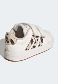 Sneaker bianca con dettagli in stampa leopardata marrone chiaro, cinturini in Velcro e suola in gomma con texture. Presenta il marchio "adidas" sul retro.