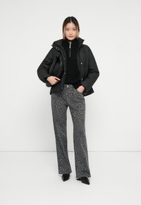 Svart pufferjakke med hette over en svart genser, kombinert med grå leopardmønstret flared bukser og svarte hæler.