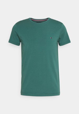 Grøn T-shirt med korte ærmer og rund halsudskæring, med lille rektangulært logo på venstre bryst, vist mod en ensartet lys baggrund.