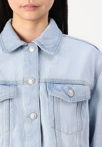 Hele hall denim jakk, millel on terav krae, hõbedased nööbid, kaks rinna taskut ja struktuurne disain. Pehme tekstuur, vabaaja stiil.