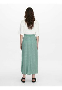 Lang, vloeiende groene rok met een witte bloemmotief, gecombineerd met een witte top met korte mouwen. Het ontwerp heeft een tailleband en een zijsplit.