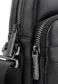 Borsa in pelle nera con superficie testurizzata, ferrature argentate, doppie cerniere e tracolla in tessuto con etichetta logo.