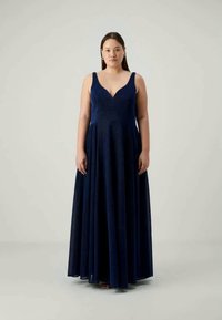 Ναυτικό μπλε, μακριά evening gown με V-λαιμόκοψη, φαρδιές τιράντες και φούστα με κλος. Το ύφασμα έχει μια διακριτική υφή.