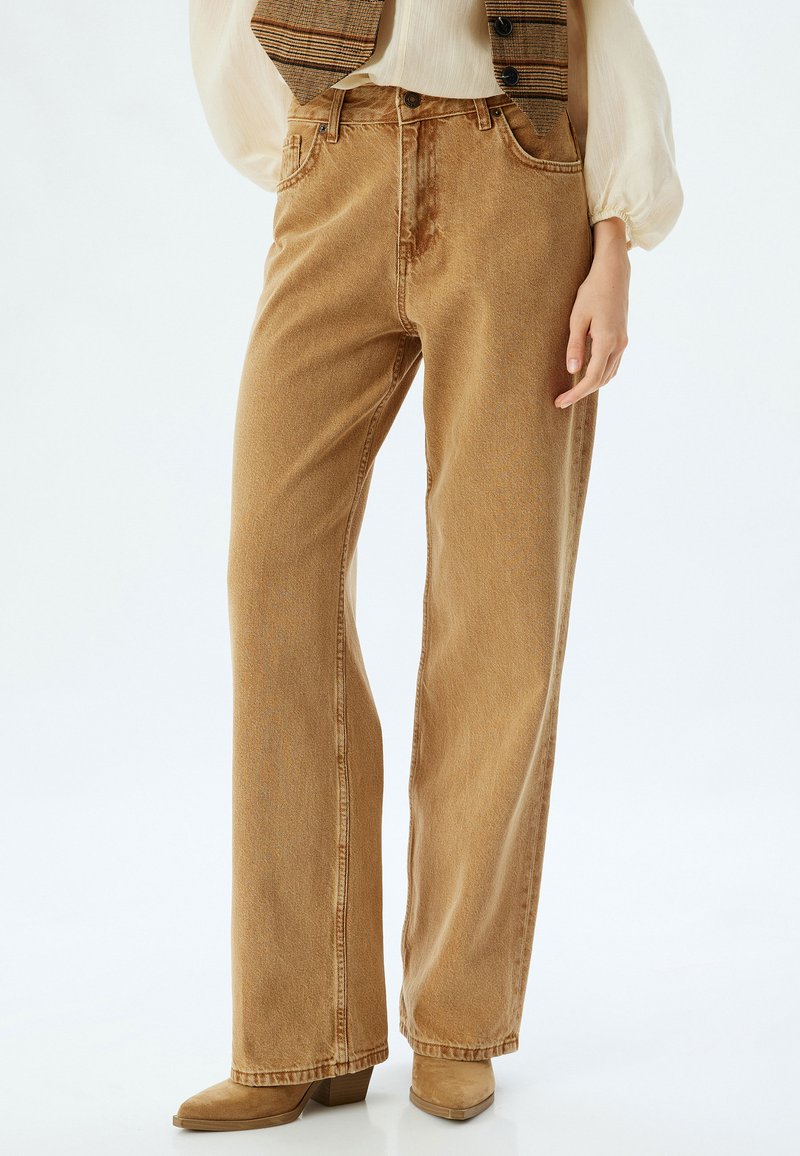 Jeans de pierna recta de color marrón claro, hechos de mezclilla, con bolsillos frontales, passantes para cinturón y una textura ligeramente deslavada.