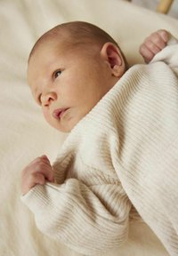 Morbidissimo avvolgimento in tessuto beige a coste con un primo piano della mano e del viso di un bambino. Uno sfondo neutro e contorni delicati mettono in risalto il design.