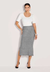 Grijze gebreide midi-skirt met kabelbreipatroon, zijsplit en geribbelde zoom. Gecombineerd met een strakke witte top en zwarte hakken.