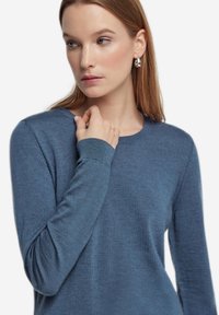 Blå tröja med långa ärmar i mjukt material, med rund halsringning och ribbade ärmslut för textur. Slät yta med minimal detaljering.