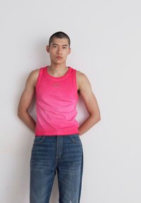 Pink ribbed tank top with a round neckline, paired with faded blue jeans. Simple design with no patterns or additional accents.