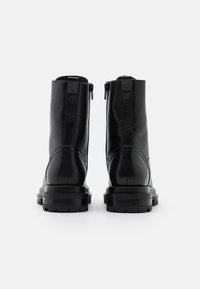 Bottes chevilles en cuir noir à finition lisse, avec une fermeture éclair à l'arrière et une semelle épaisse pour plus de stabilité.