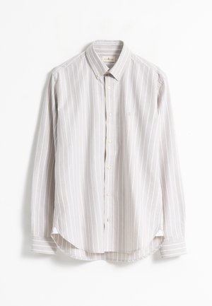 Camisa de botones de manga larga color beige con rayas verticales blancas, con cuello abotonado y dobladillo redondeado, dispuesta plana sobre un fondo blanco.