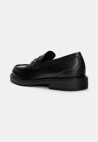 Mocassini in pelle nera con punta arrotondata, cuciture decorative e una spessa suola in gomma. Presentano un design slip-on e dettagli minimi.