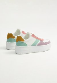 Zapatillas de plataforma blancas con acentos en tonos pastel de rosa, verde y púrpura; presentan una mezcla de texturas de cuero y ante. Suela robusta de goma.