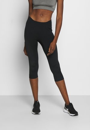 Leggings capri noirs en tissu extensible, avec des panneaux latéraux texturés, une taille haute et associés à des chaussures de sport noires.