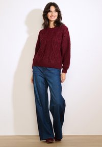 Bordowy sweter z dzianiny z fakturowanym wzorem warkocza, okrągłym dekoltem i długimi rękawami, w połączeniu z szerokimi niebieskimi jeansami dżinsowymi.