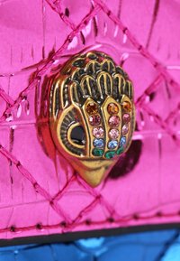 Pink, glossy leather with a quilted pattern, featuring a decorative gold-toned clasp adorned with colorful rhinestones and detailing.