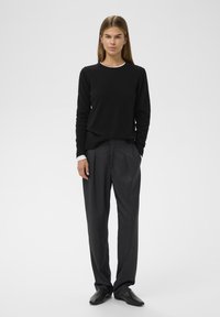 Zwarte gebreide trui met een ronde halslijn, gecombineerd met donkergrijze geplooide broek en zwarte schoenen, die een eenvoudige, op maat gemaakte uitstraling laten zien.