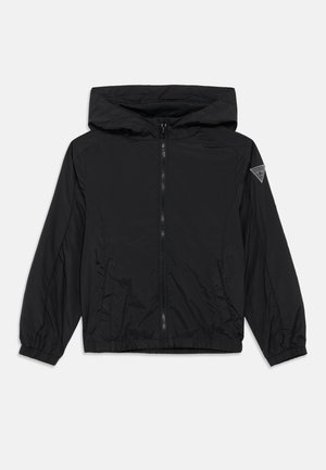 Chaqueta negra con capucha y cremallera, puños y dobladillo elásticos, dos bolsillos delanteros y un pequeño parche con logo triangular en la manga izquierda.