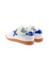 Zapatillas blancas con parte superior perforada, acentos en azul y amarillo, y suela de goma. Presenta el logotipo en el talón y una 'X' estilizada.