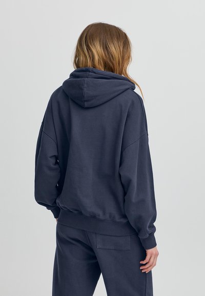 Felpa oversize blu navy con un ampio cappuccio, polsini e orlo a coste, e tessuto morbido e texturizzato. Presenta una vestibilità rilassata e un design minimale.